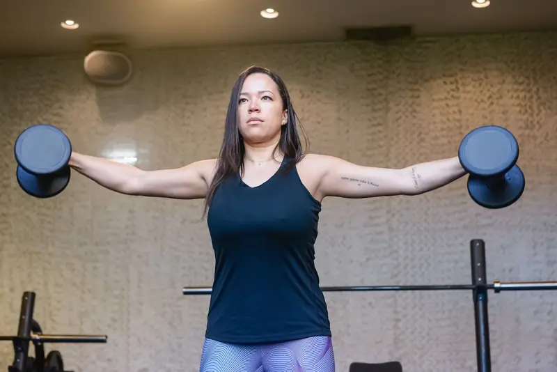 Mulher fazendo elevação lateral com halteres na academia
